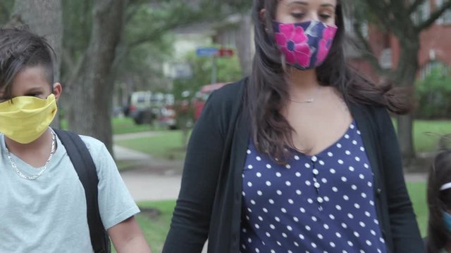 Prerequisite for in classroom instruction and the new normal during COVID19 pandemic is mask wearing as demonstrated by this mother and her children as she walks them to the school bus stop.