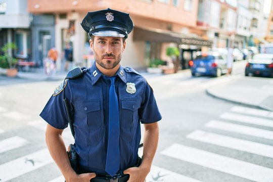 young handsome hispanic policeman wearing police uniform. Standing with serious expression at town street.