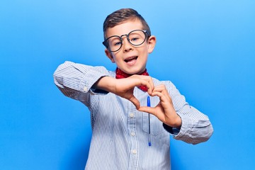 Fototapeta premium Cute blond kid wearing nerd bow tie and glasses smiling in love doing heart symbol shape with hands. romantic concept.