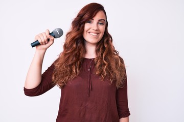 Young beautiful woman singing song using microphone looking positive and happy standing and smiling with a confident smile showing teeth