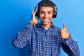 Young african amercian man listening to music using headphones smiling happy and positive, thumb up doing excellent and approval sign