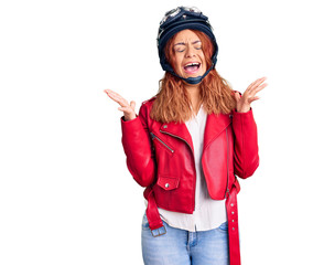 Young latin woman wearing leather jacket holding motorcycle helmet celebrating mad and crazy for success with arms raised and closed eyes screaming excited. winner concept