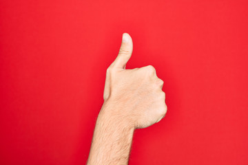 Hand of caucasian young man showing fingers over isolated red background doing successful approval gesture with thumbs up, validation and positive symbol