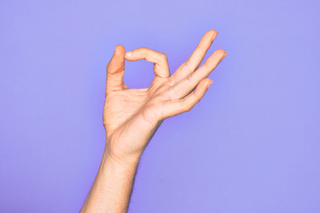 Hand of caucasian young man showing fingers over isolated purple background gesturing approval...