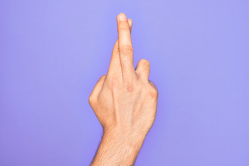 Hand of caucasian young man showing fingers over isolated purple background gesturing fingers crossed, superstition and lucky gesture, lucky and hope expression