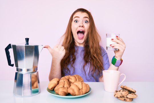 Young redhead woman eating breakfast pointing finger up with successful idea. exited and happy. number one.