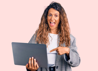 Young hispanic woman with tattoo holding laptop smiling happy pointing with hand and finger