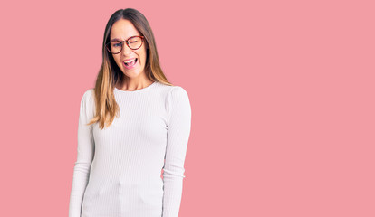 Beautiful brunette young woman wearing casual white sweater and glasses winking looking at the...