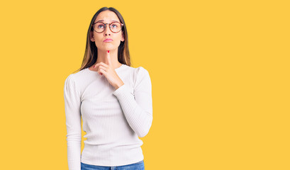Beautiful brunette young woman wearing casual white sweater and glasses thinking concentrated about...