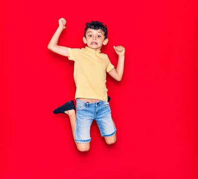 Adorable kid wearing casual clothes jumping over isolated red background