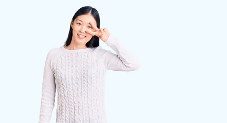 Young beautiful chinese woman wearing casual sweater doing peace symbol with fingers over face, smiling cheerful showing victory