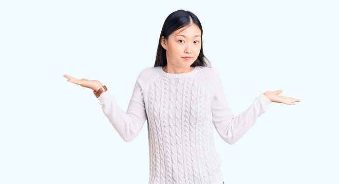 Young beautiful chinese woman wearing casual sweater clueless and confused expression with arms and hands raised. doubt concept.