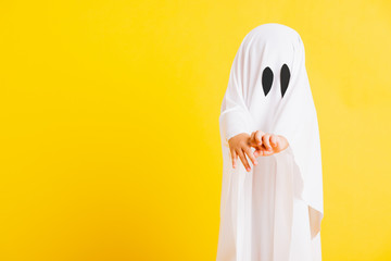 Funny Halloween Kid Concept, Closeup a little cute child with white dressed costume halloween ghost scary, studio shot isolated on yellow background