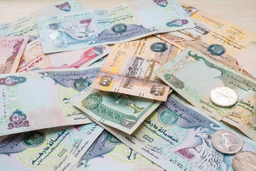 Closeup of different UAE dirhams currency notes and coins , paper money on a light wooden table from high angle