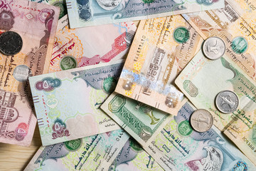 Closeup of different UAE dirhams currency notes and coins , paper money on a light wooden table from high angle