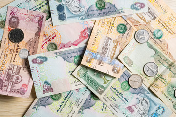 Closeup of different UAE dirhams currency notes and coins , paper money on a light wooden table from high angle