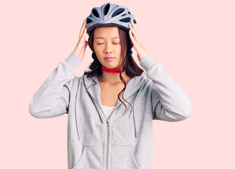 Young beautiful chinese girl wearing bike helmet suffering from headache desperate and stressed because pain and migraine. hands on head.