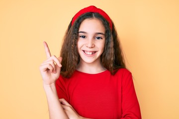 Cute hispanic child girl wearing casual clothes and diadem with a big smile on face, pointing with hand and finger to the side looking at the camera.