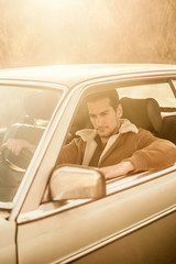 A handsome man driving an oldtimer car travels into the sunset