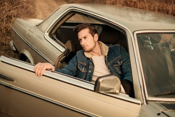 A handsome man driving an oldtimer car travels into the sunset