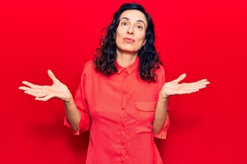 Young beautiful hispanic woman wearing casual clothes clueless and confused expression with arms...