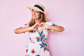 Middle age hispanic woman wearing summer hat smiling in love showing heart symbol and shape with hands. romantic concept.