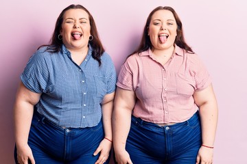 Young plus size twins wearing casual clothes sticking tongue out happy with funny expression. emotion concept.