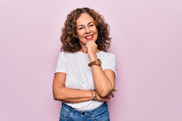 Middle age beautiful woman wearing casual t-shirt standing over isolated pink background smiling looking confident at the camera with crossed arms and hand on chin. Thinking positive.