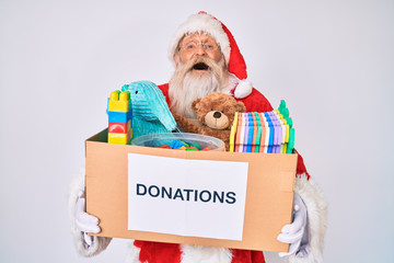 Old senior man wearing santa claus costume holding donation box smiling and laughing hard out loud...