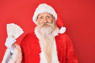 Old senior man with grey hair and long beard wearing santa claus costume holding pounds looking positive and happy standing and smiling with a confident smile showing teeth
