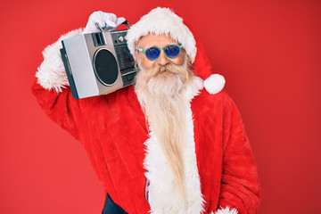 Old senior man wearing santa claus costume and boombox looking positive and happy standing and smiling with a confident smile showing teeth
