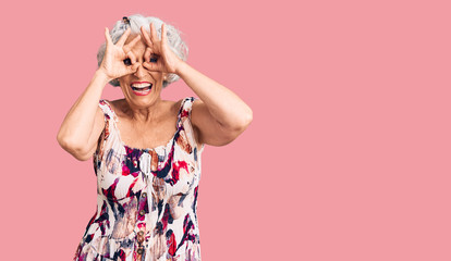 Senior grey-haired woman wearing casual clothes doing ok gesture like binoculars sticking tongue out, eyes looking through fingers. crazy expression.