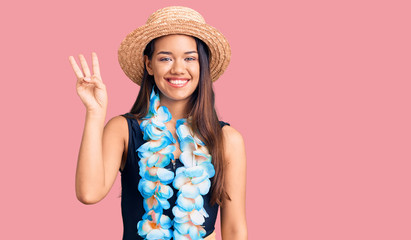 Young beautiful latin girl wearing hawaiian lei and summer hat showing and pointing up with fingers number three while smiling confident and happy.