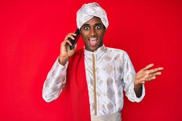 Indian man wearing tradition sherwani saree clothes speaking on the phone celebrating achievement...