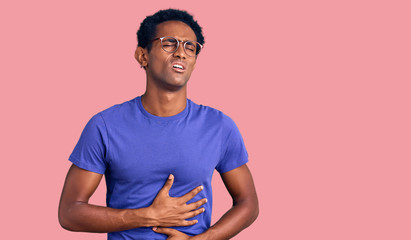 African handsome man wearing casual clothes and glasses with hand on stomach because nausea, painful disease feeling unwell. ache concept.