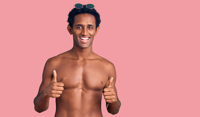 Fototapeta premium African handsome man wearing swimsuit and sunglasses success sign doing positive gesture with hand, thumbs up smiling and happy. cheerful expression and winner gesture.
