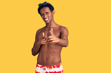 Fototapeta premium African handsome man wearing swimsuit and sunglasses pointing fingers to camera with happy and funny face. good energy and vibes.