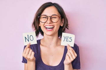 Young beautiful girl holding yes and no reminder smiling and laughing hard out loud because funny...