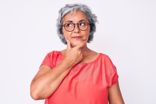 Senior hispanic grey- haired woman wearing casual clothes and glasses with hand on chin thinking about question, pensive expression. smiling with thoughtful face. doubt concept.