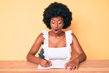 Fototapeta na wymiar Young african american woman writing book scared and amazed with open mouth for surprise, disbelief face