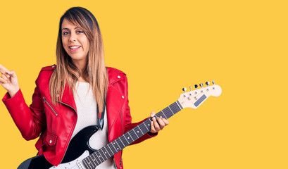 Fototapeta premium Young beautiful woman playing electric guitar smiling happy pointing with hand and finger to the side