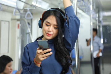 A lifestyle of young Asian woman using cellphone with headset while taking the subway train to work at the rush hour morning with copy space