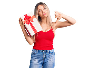 Young beautiful blonde woman holding gift with angry face, negative sign showing dislike with thumbs down, rejection concept