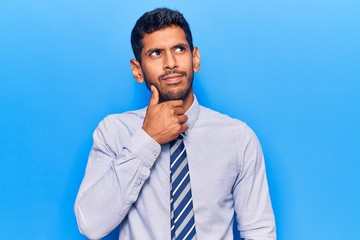 Young latin man wearing business clothes serious face thinking about question with hand on chin, thoughtful about confusing idea