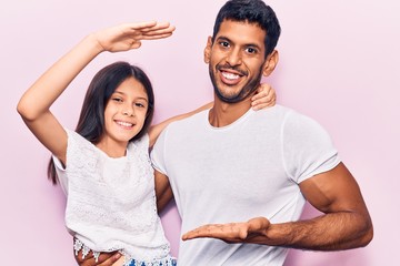 Young father and daughter wearing casual clothes gesturing with hands showing big and large size sign, measure symbol. smiling looking at the camera. measuring concept.