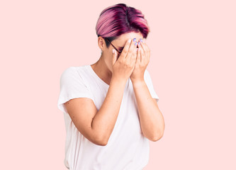 Young beautiful woman with pink hair wearing casual clothes and glasses with sad expression covering face with hands while crying. depression concept.