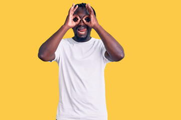 Fototapeta premium Young african american man with braids wearing casual white tshirt doing ok gesture like binoculars sticking tongue out, eyes looking through fingers. crazy expression.