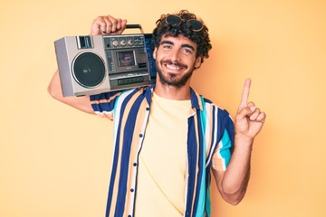 Handsome young man with curly hair and bear holding boombox, listening to music wearing summer look...