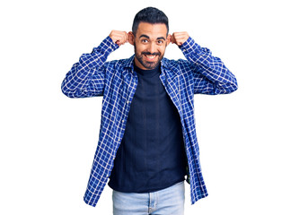 Young hispanic man wearing casual clothes smiling pulling ears with fingers, funny gesture....