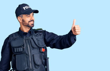 Fototapeta premium Young hispanic man wearing police uniform looking proud, smiling doing thumbs up gesture to the side